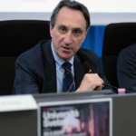 Il Magnifico Rettore dell'Università del Piemonte Orientale Menico Rizzi mentre parla al microfono seduto al tavolo.